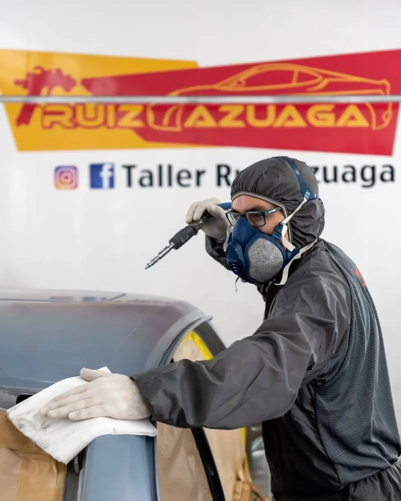 Operario puliendo la carrocería de un coche en la cabina del taller en Málaga